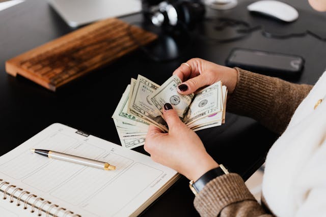 Person counting money in front of a pen and paper